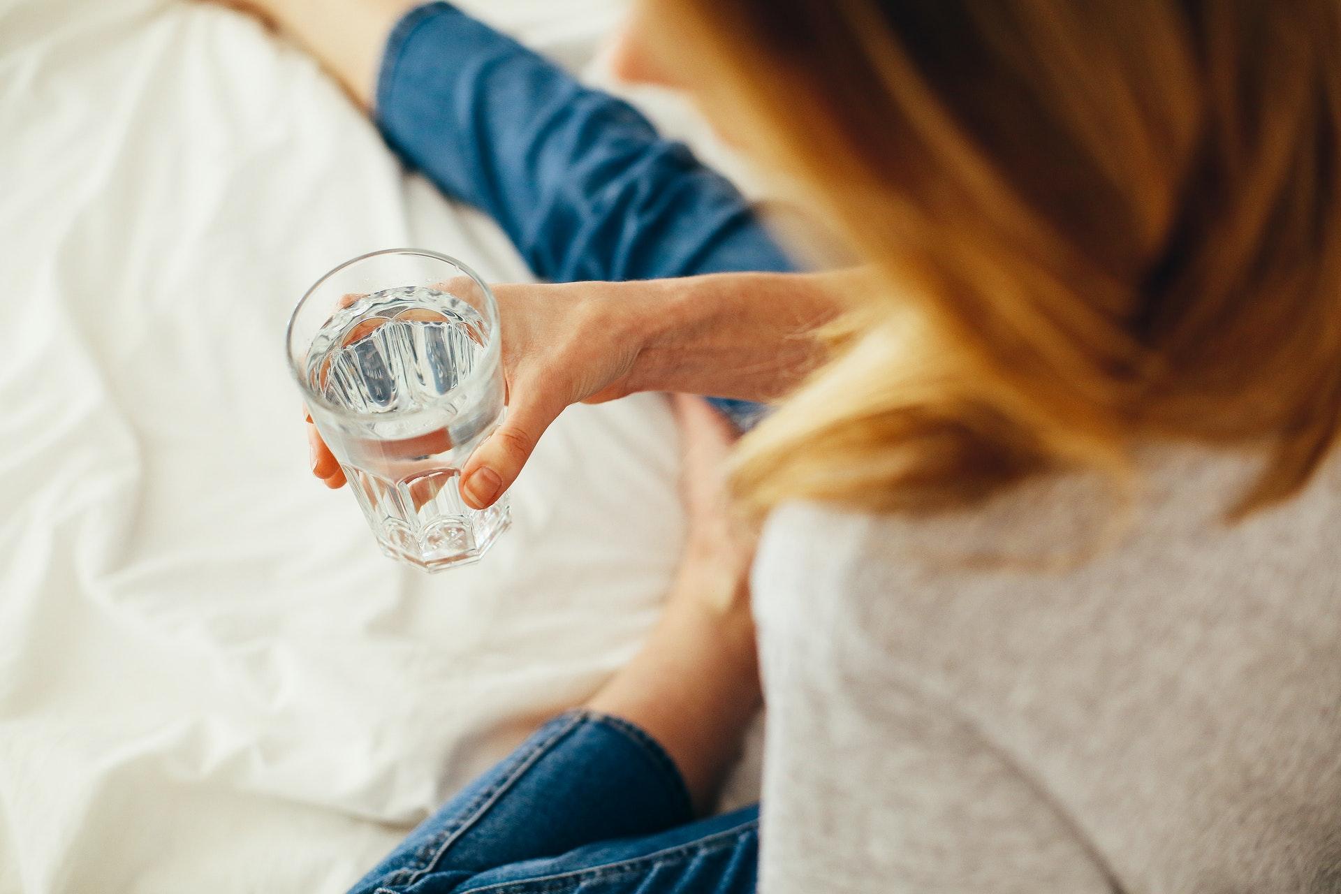 woman-holding-glass-of-water-in-hand-laying-on-bed.jpg